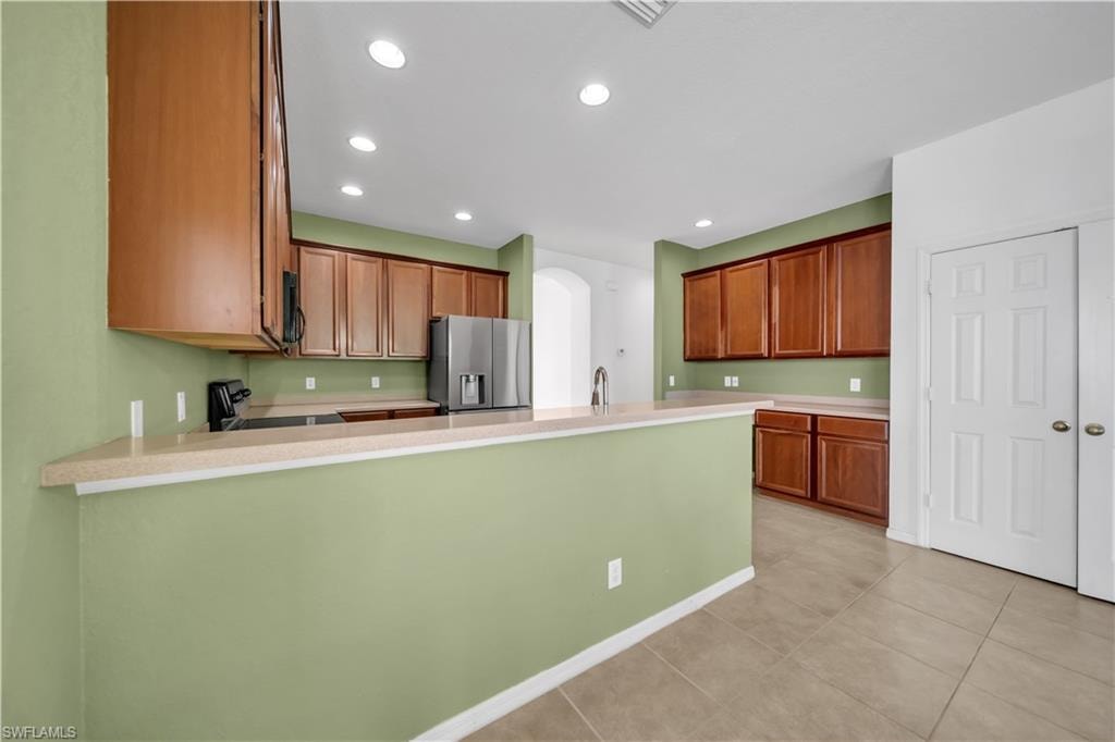 Kitchen featuring brown cabinets, recessed lighting, stainless steel refrigerator with ice dispenser, arched walkways, and light countertops