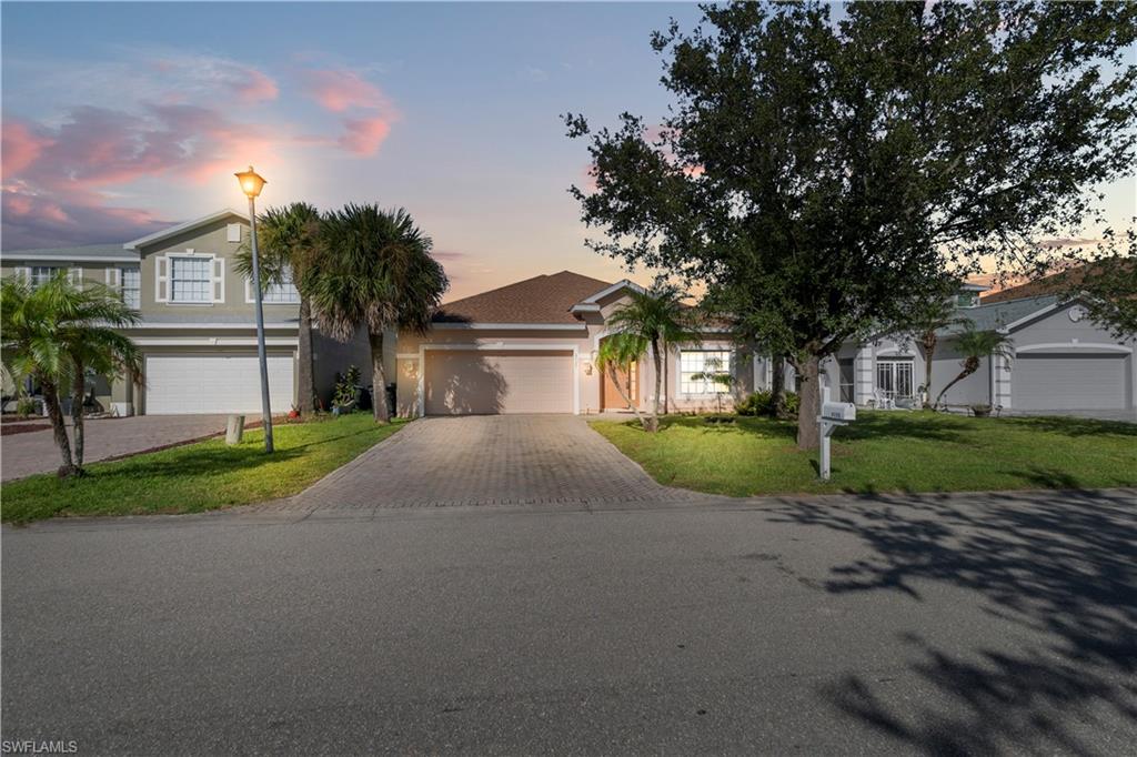 View of front of property with decorative driveway, a yard, and stucco siding