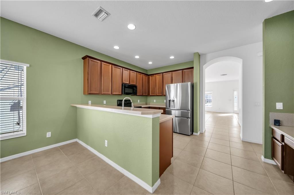 Kitchen with arched walkways, black appliances, light tile patterned floors, recessed lighting, and a peninsula