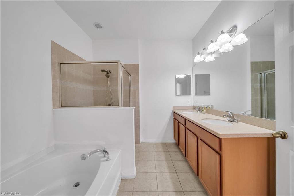 Bathroom featuring light tile patterned floors, a bath, double vanity, and a shower stall