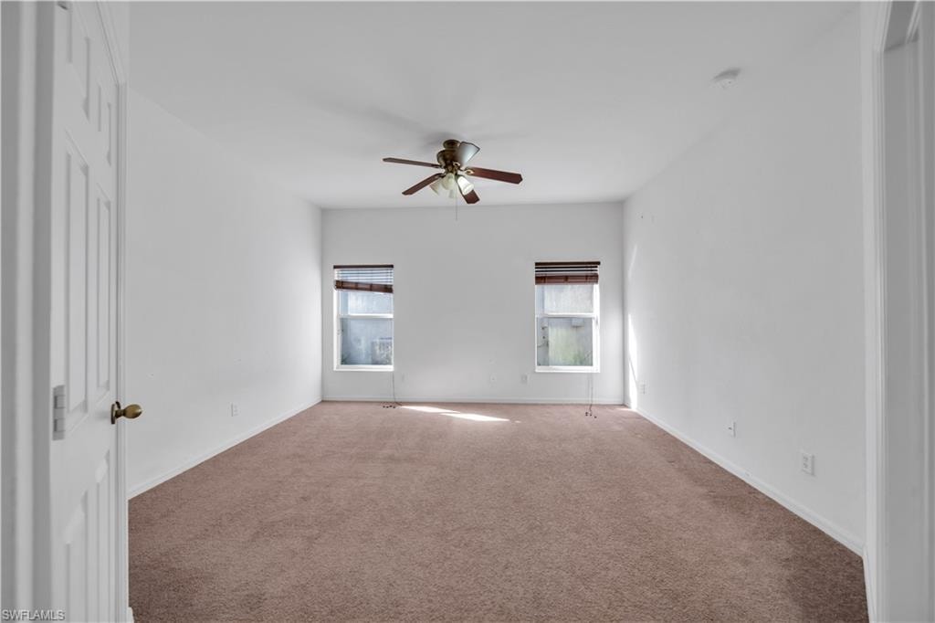 Carpeted empty room with ceiling fan and baseboards