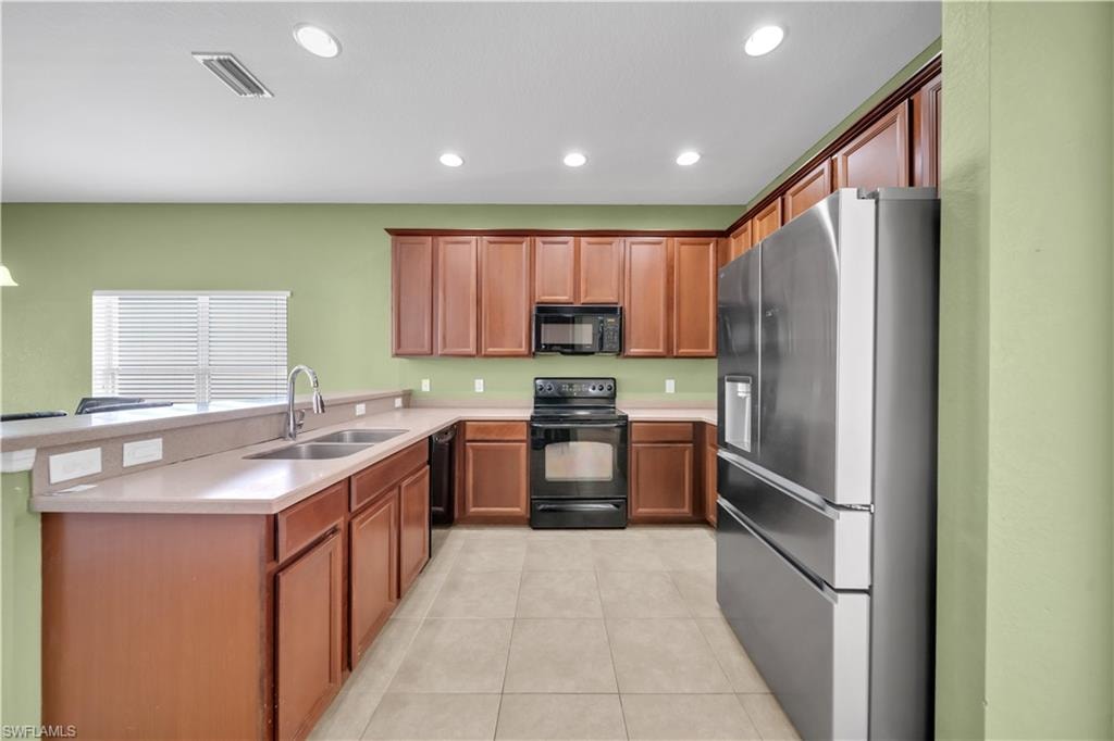 Kitchen featuring black appliances, brown cabinetry, light tile patterned floors, recessed lighting, and a peninsula