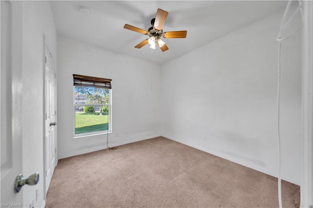 Carpeted spare room with ceiling fan and baseboards