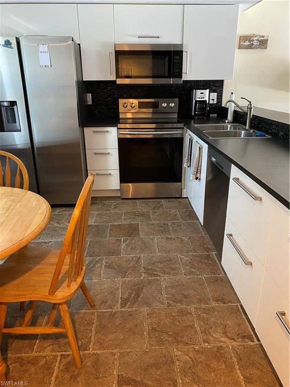Kitchen featuring appliances with stainless steel finishes, dark countertops, white cabinetry, backsplash, and modern cabinets