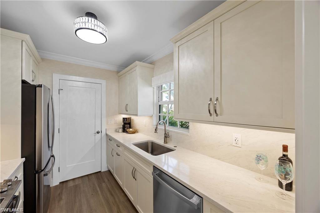 Kitchen featuring stainless steel appliances, ornamental molding, light stone counters, dark wood finished floors, and decorative backsplash