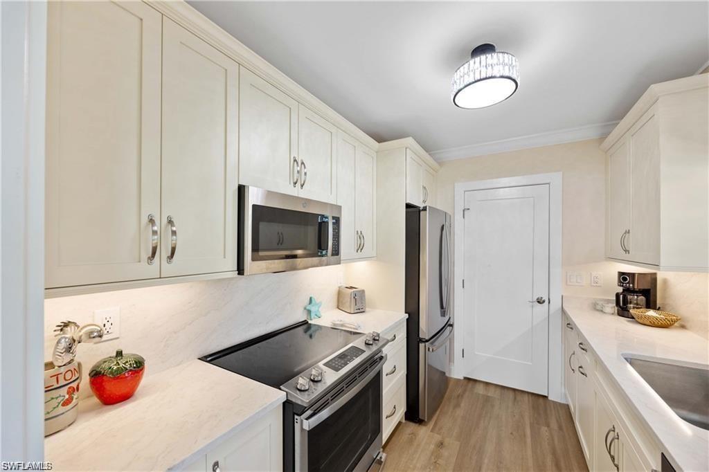 Kitchen with stainless steel appliances, light wood-type flooring, light stone counters, crown molding, and white cabinetry