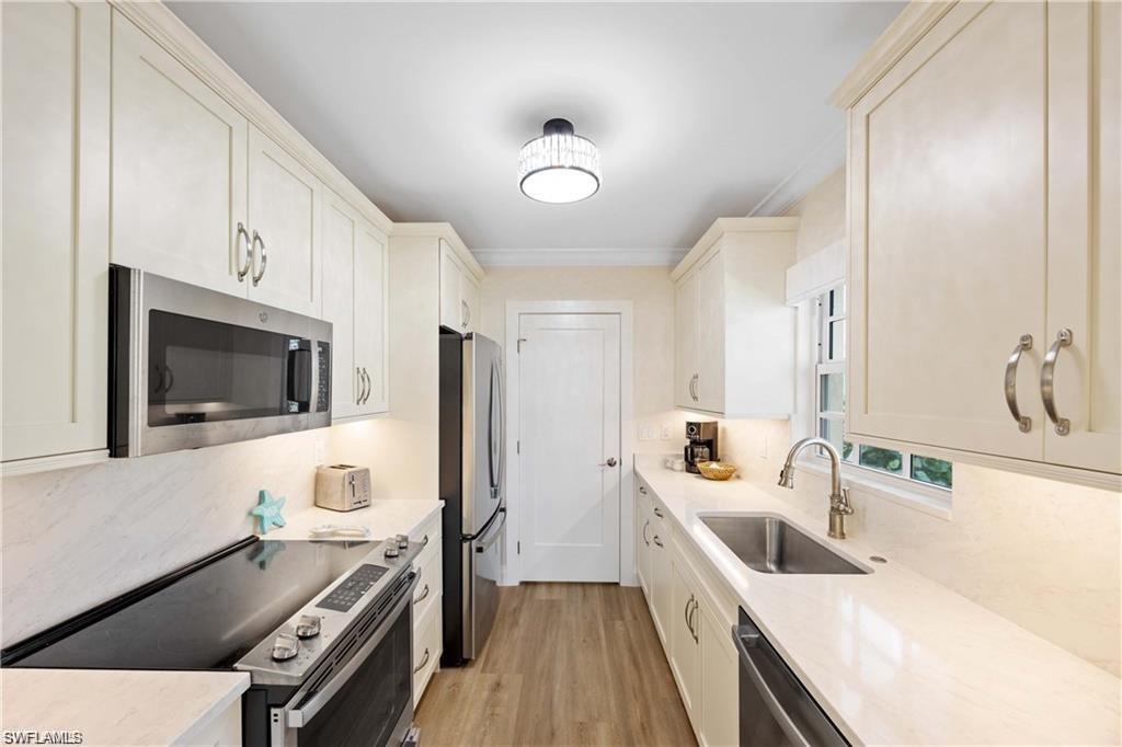 Kitchen with stainless steel appliances, light stone counters, light wood-style flooring, and ornamental molding