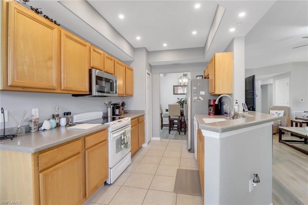 Kitchen with white electric range oven, stainless steel microwave, light brown cabinetry, recessed lighting, and light tile patterned floors