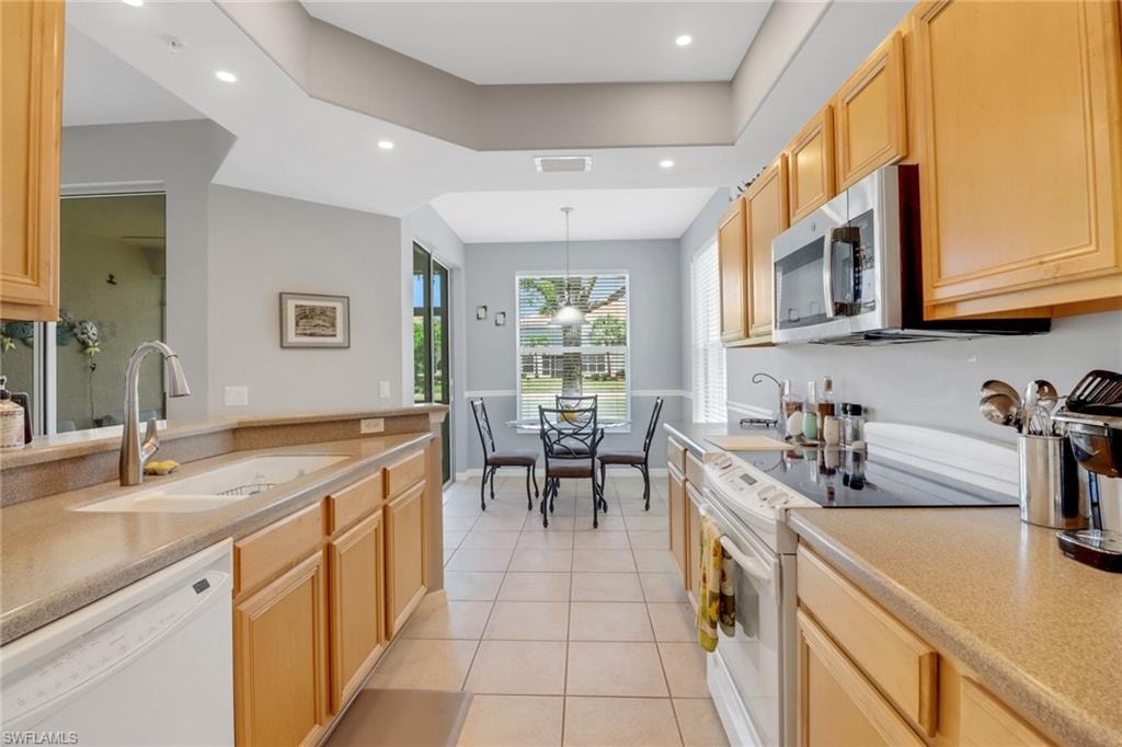 Kitchen with white appliances, light brown cabinets, light tile patterned floors, pendant lighting, and recessed lighting