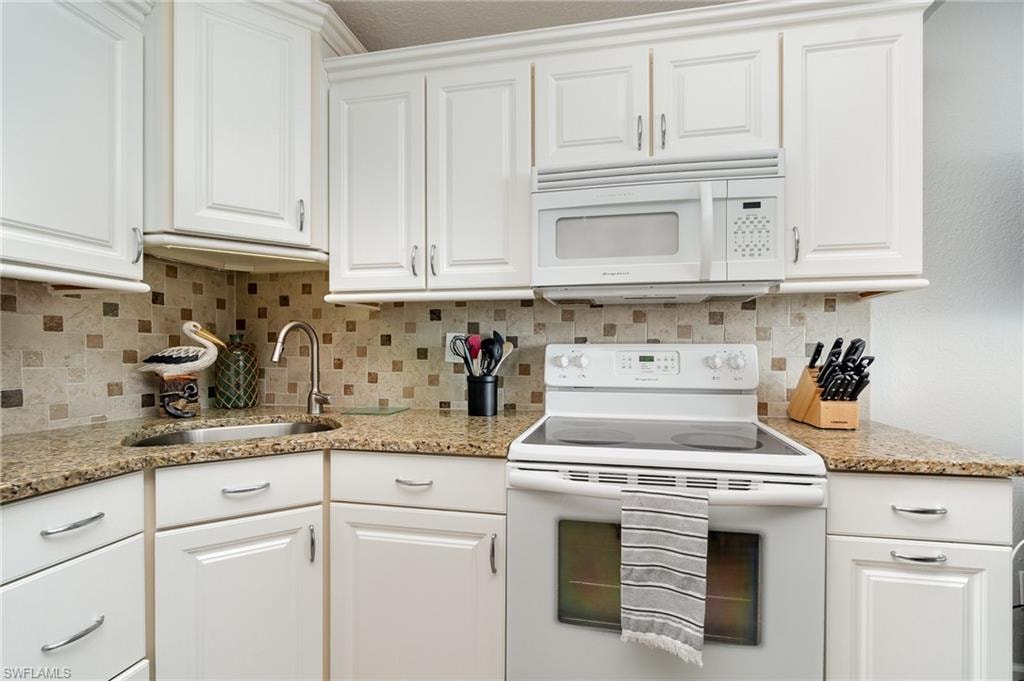 Kitchen with white appliances, white cabinetry, granite countertops, and decorative backsplash