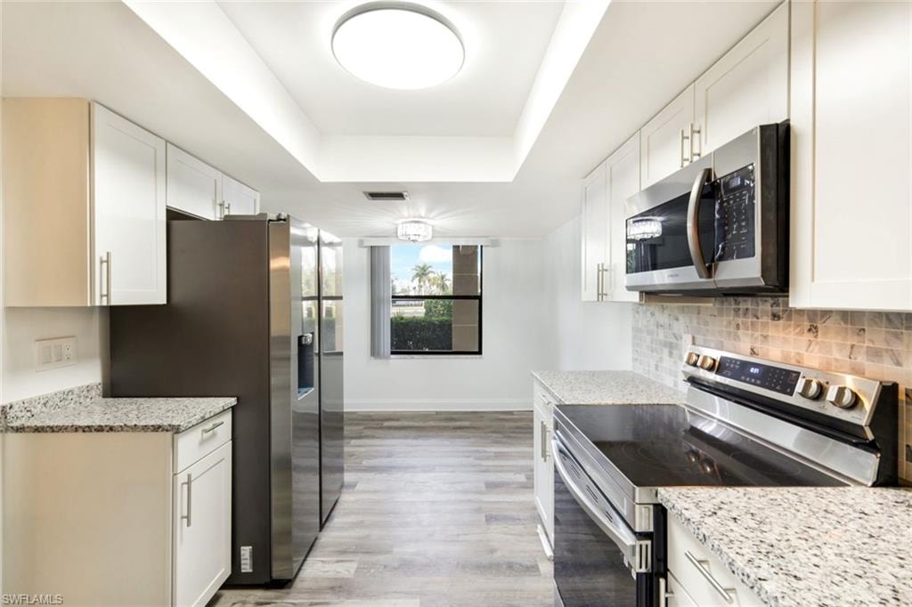 Kitchen featuring a raised ceiling, appliances with stainless steel finishes, light stone countertops, and white cabinets