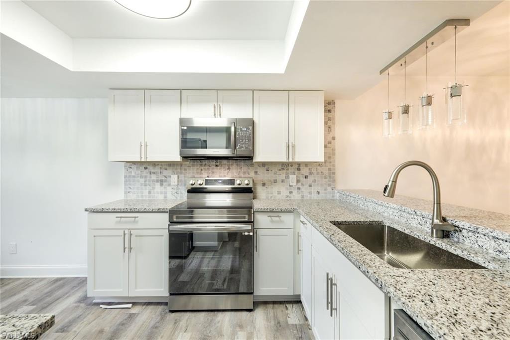 Kitchen with stainless steel appliances, white cabinets, decorative backsplash, decorative light fixtures, and light stone counters