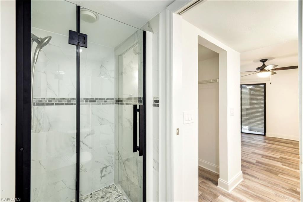 Full bath featuring a ceiling fan, a marble finish shower, light wood finished floors, and a spacious closet