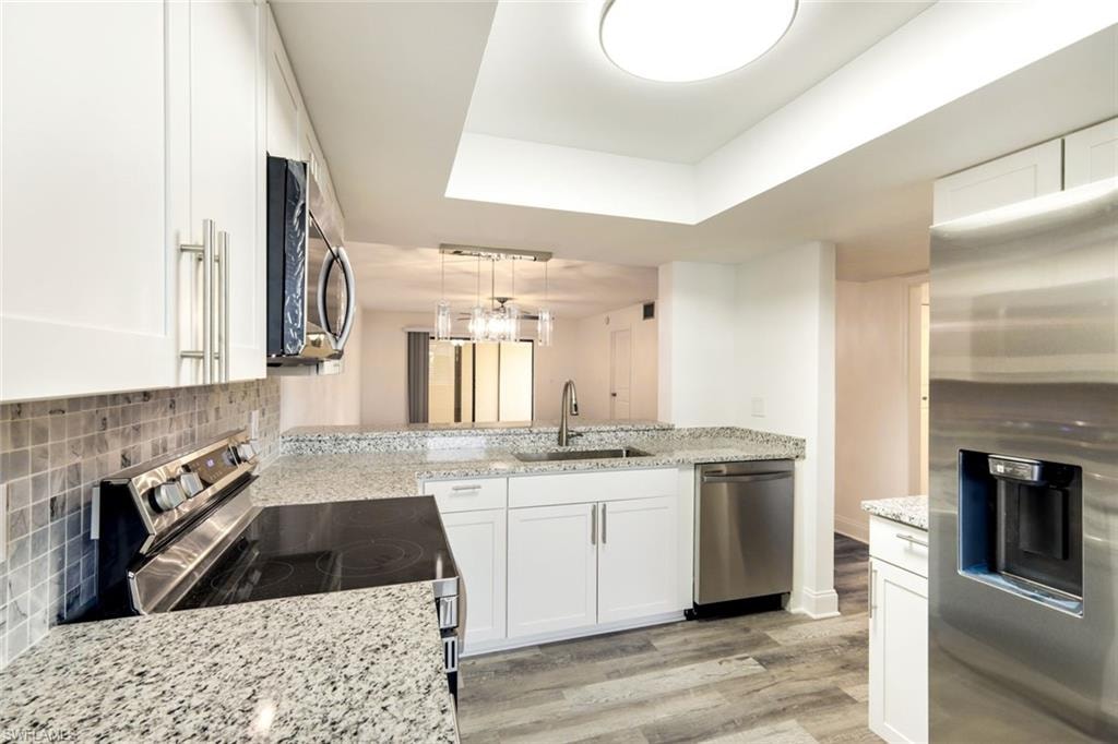 Kitchen featuring appliances with stainless steel finishes, white cabinetry, light stone counters, and light wood finished floors