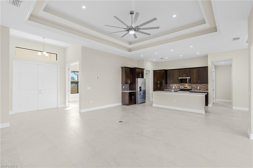 Unfurnished living room with a raised ceiling, recessed lighting, a ceiling fan, and light tile patterned flooring