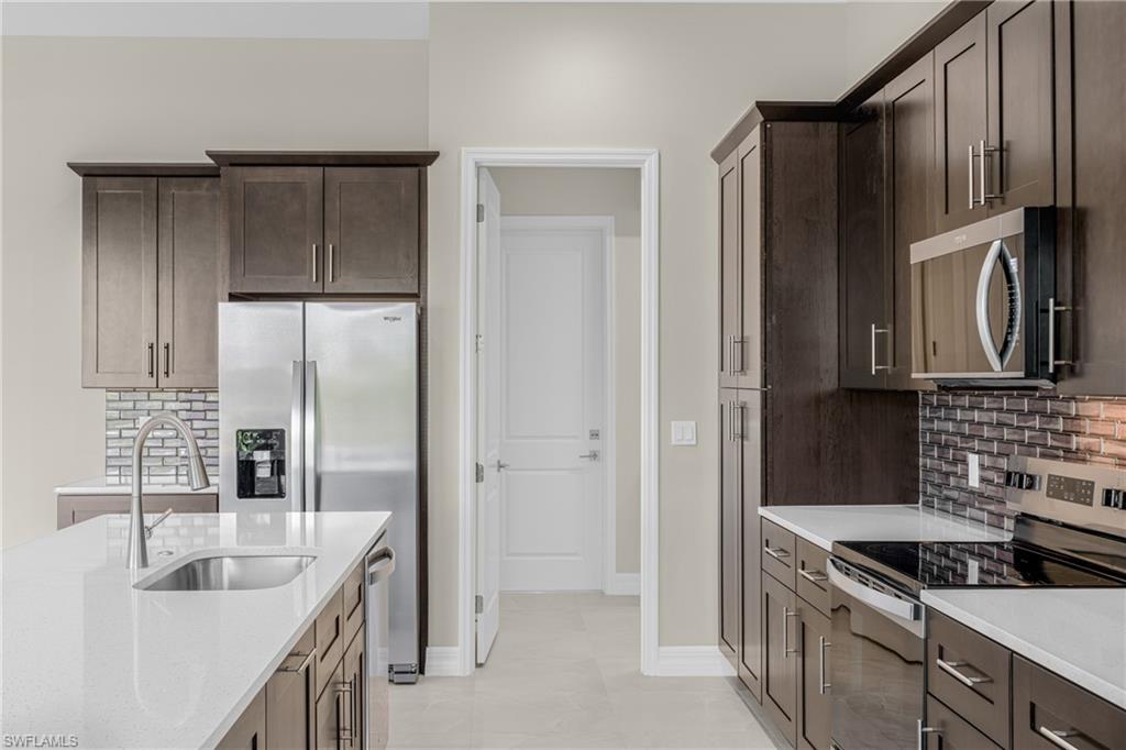 Kitchen with decorative backsplash, appliances with stainless steel finishes, dark brown cabinets, light stone countertops, and light tile patterned floors