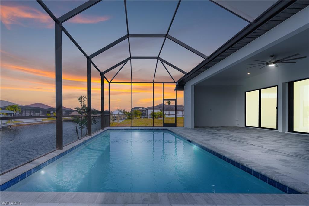 Swimming pool featuring a sunroom, ceiling fan, glass enclosure, a patio, and a water view