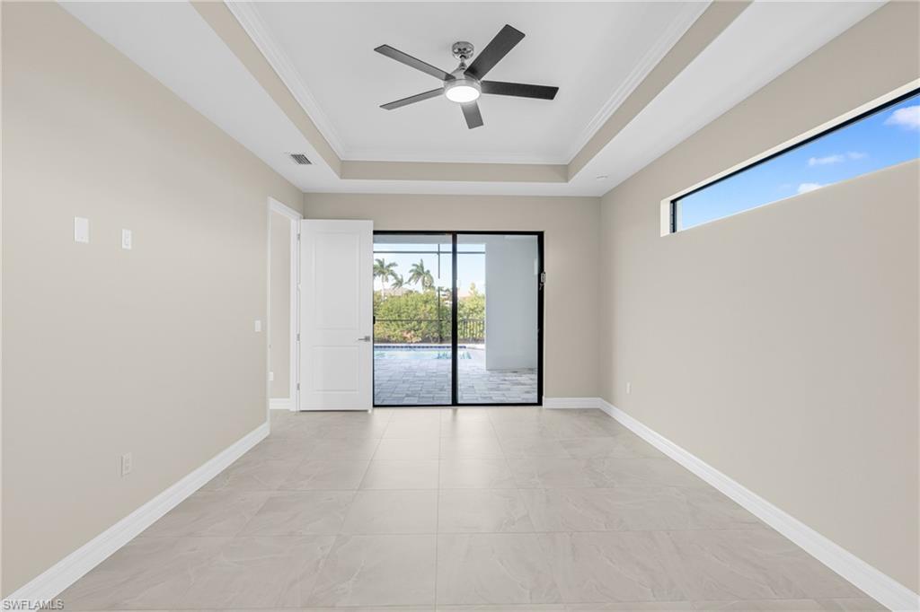 Empty room featuring ornamental molding, a raised ceiling, a ceiling fan, and light tile patterned flooring