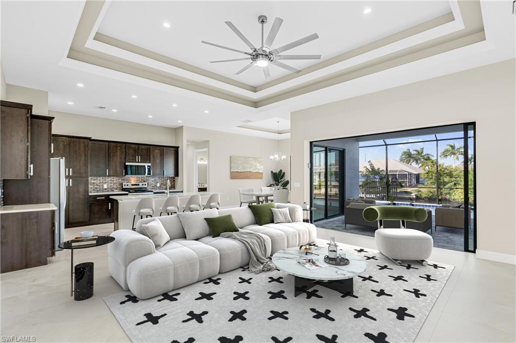Living area featuring a tray ceiling, ceiling fan, recessed lighting, light tile patterned floors, and a chandelier