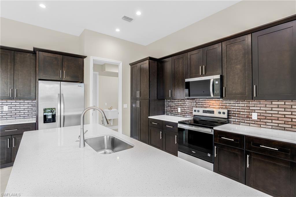 Kitchen featuring dark brown cabinets, decorative backsplash, appliances with stainless steel finishes, light stone countertops, and recessed lighting