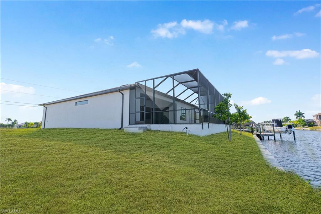 Back of house featuring a sunroom, a lawn, glass enclosure, stucco siding, and a water view