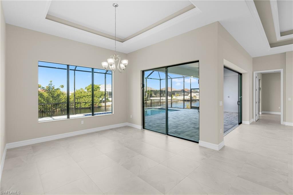 Spare room featuring a raised ceiling, a chandelier, light tile patterned floors, a sunroom, and a water view