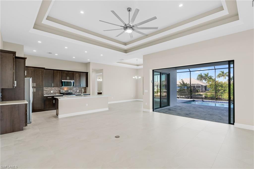Unfurnished living room featuring a tray ceiling, a ceiling fan, recessed lighting, and a chandelier