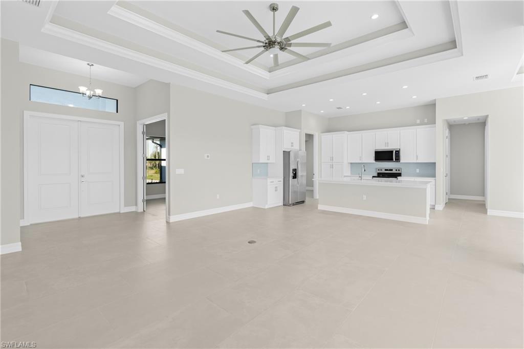 Unfurnished living room featuring a raised ceiling, a chandelier, and ceiling fan