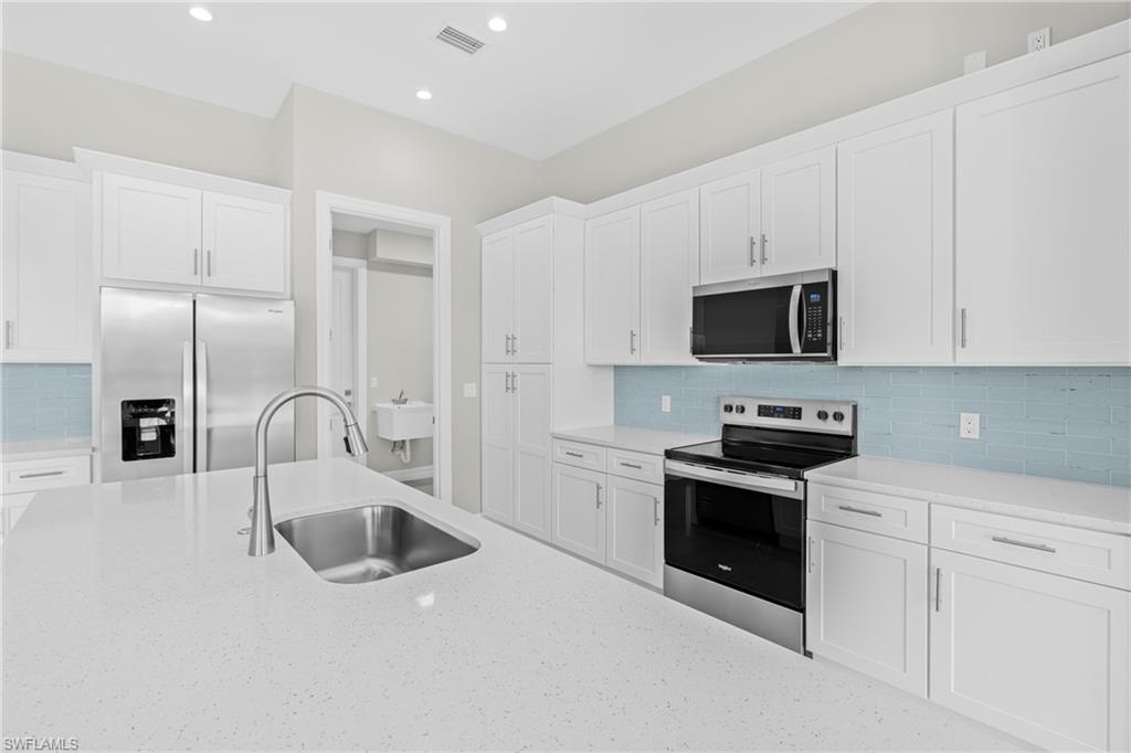 Kitchen with appliances with stainless steel finishes, backsplash, white cabinetry, light stone counters, and recessed lighting
