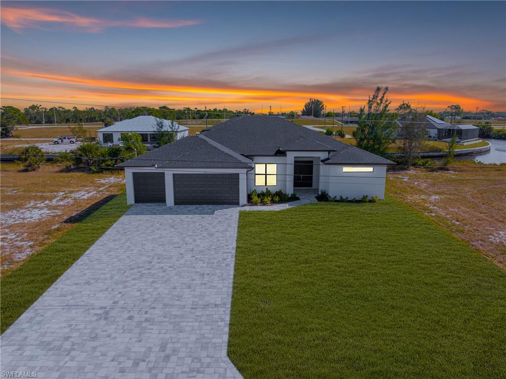 View of front facade with decorative driveway, a front lawn, an attached garage, and roof with shingles
