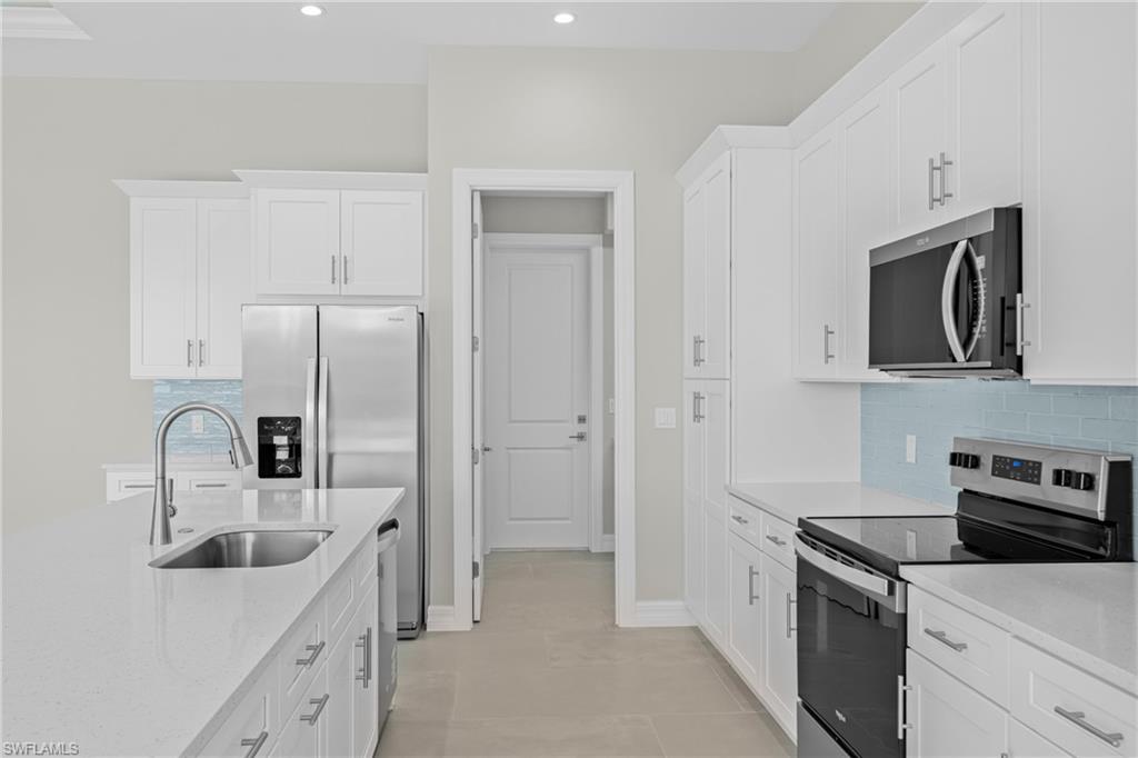 Kitchen with appliances with stainless steel finishes, decorative backsplash, white cabinetry, light stone countertops, and recessed lighting