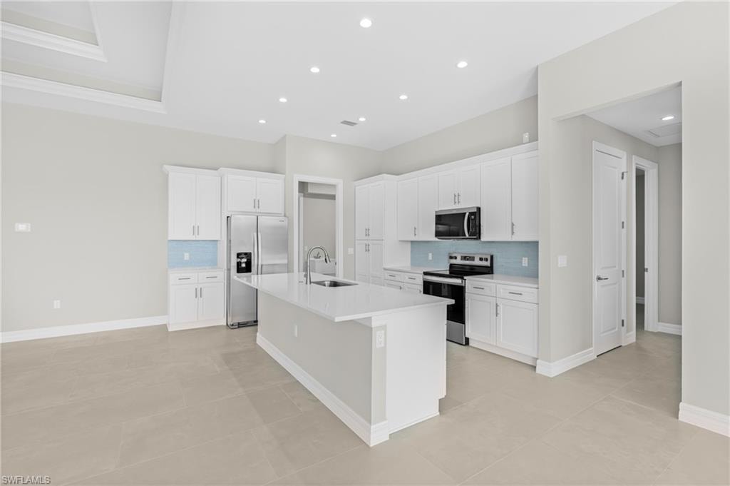Kitchen with decorative backsplash, appliances with stainless steel finishes, white cabinets, a center island with sink, and recessed lighting