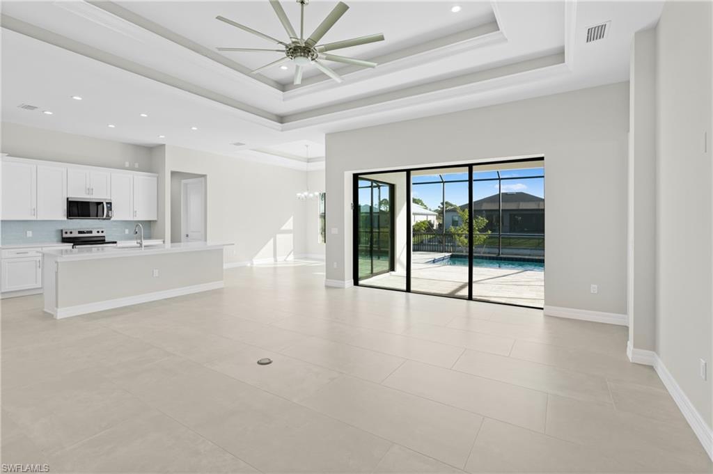 Unfurnished living room with a raised ceiling, recessed lighting, a chandelier, a ceiling fan, and light tile patterned floors