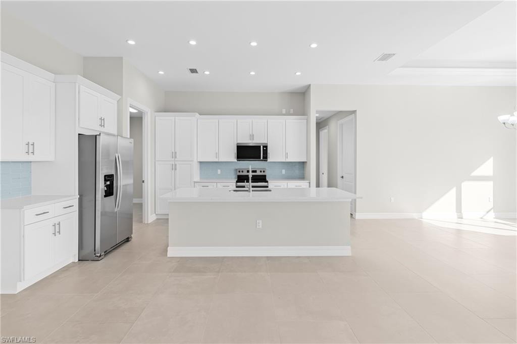 Kitchen featuring tasteful backsplash, appliances with stainless steel finishes, white cabinetry, a center island with sink, and light stone counters