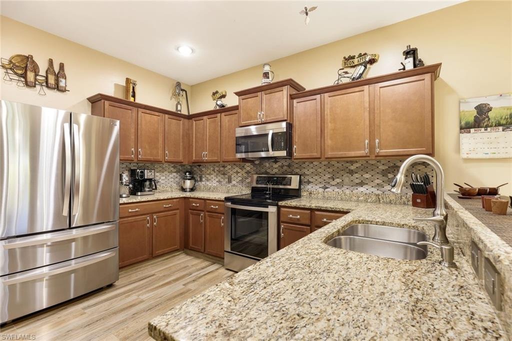 Kitchen featuring stainless steel appliances, brown cabinetry, a peninsula, light stone countertops, and light wood-style flooring