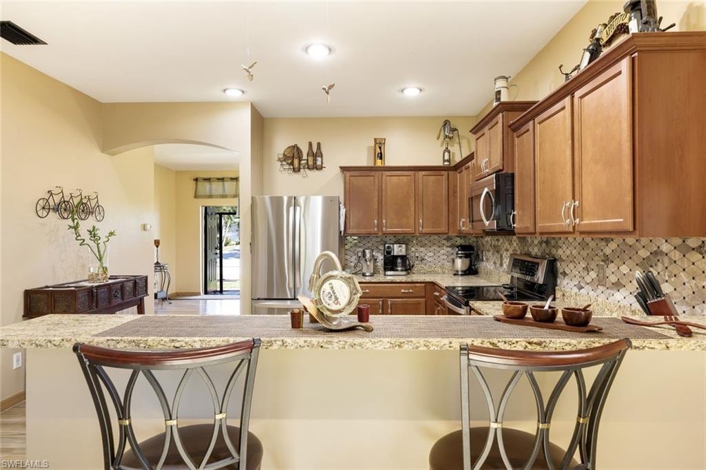 Kitchen featuring stainless steel appliances, brown cabinets, decorative backsplash, and light stone countertops