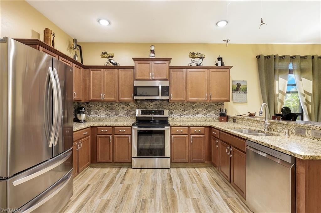 Kitchen with a peninsula, stainless steel appliances, brown cabinetry, open floor plan, and tasteful backsplash