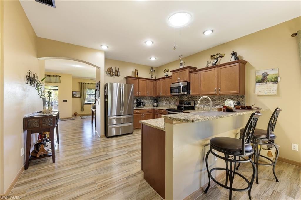 Kitchen with a kitchen breakfast bar, brown cabinetry, appliances with stainless steel finishes, and tasteful backsplash