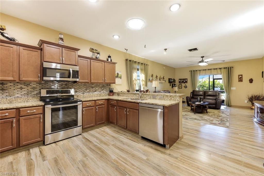 Kitchen featuring brown cabinetry, a peninsula, light stone counters, appliances with stainless steel finishes, and light wood-type flooring