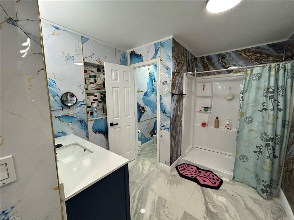 Full bath with vanity, stone wall, a stall shower, and light marble finish floors