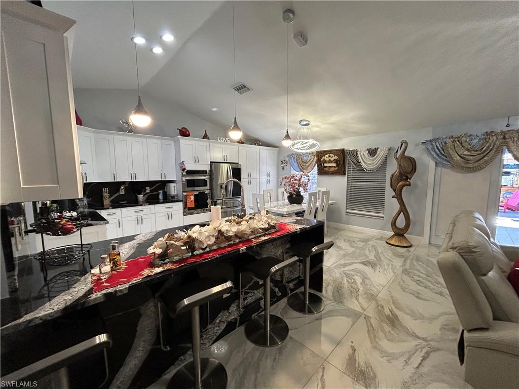 Kitchen featuring pendant lighting, a breakfast bar, white cabinetry, light marble finish floors, and backsplash