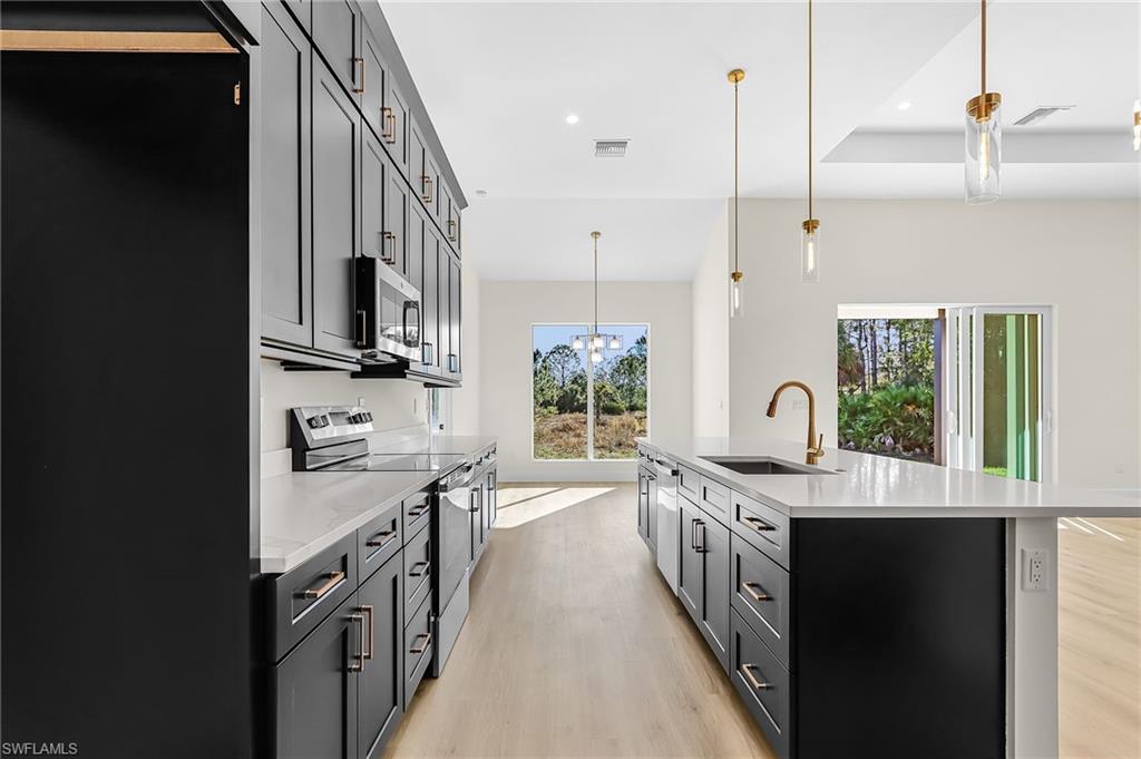Kitchen featuring stainless steel appliances, light wood-type flooring, a center island with sink, light stone countertops, and dark cabinetry