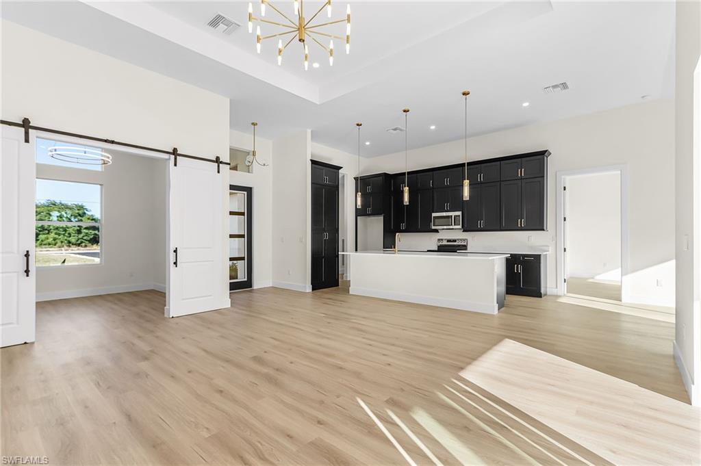 Kitchen featuring open floor plan, dark cabinets, light countertops, an island with sink, and a raised ceiling