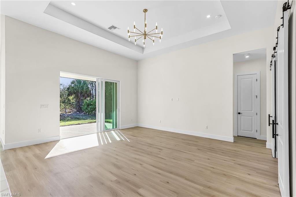 Unfurnished room with a barn door, hanging lights, a tray ceiling, and light wood-type flooring