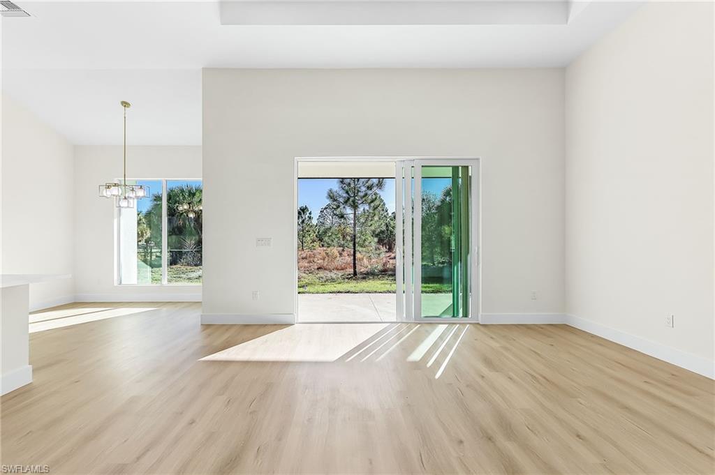 Spare room featuring a chandelier, light wood finished floors, healthy amount of natural light, and a high ceiling