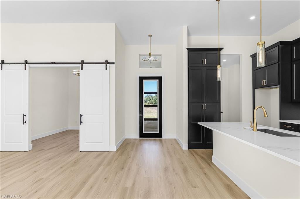 Kitchen with dark cabinetry, light stone countertops, hanging light fixtures, light wood finished floors, and a barn door