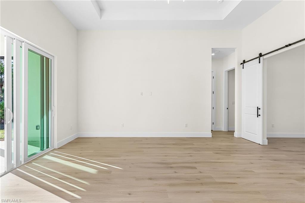 Living room, with a barn door access to office, access to exterior, light wood-style flooring, and a tray ceiling