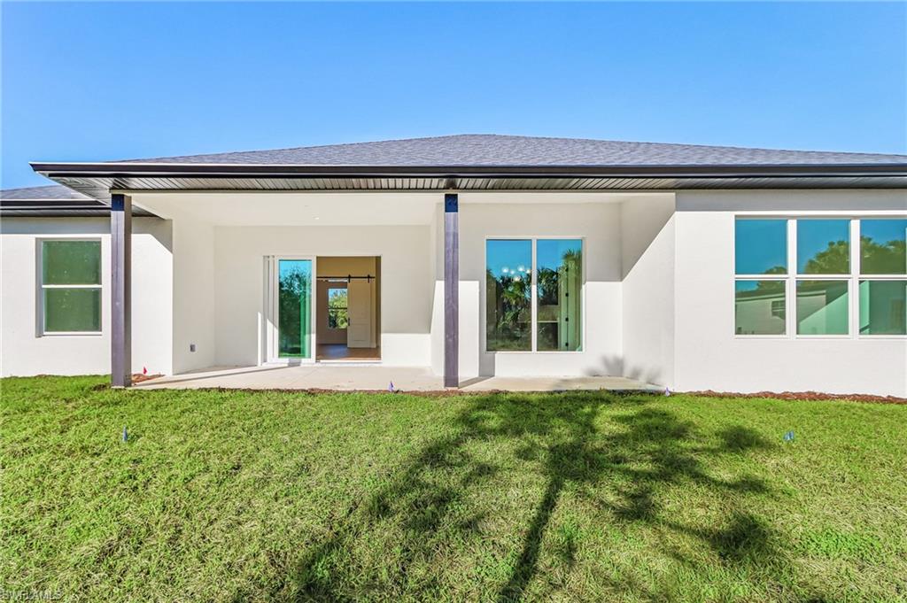 Back of property featuring stucco siding, a patio, and a lawn