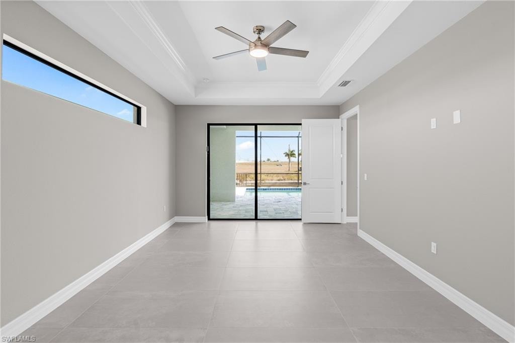 Spare room with healthy amount of natural light, a tray ceiling, a ceiling fan, crown molding, and light tile patterned floors