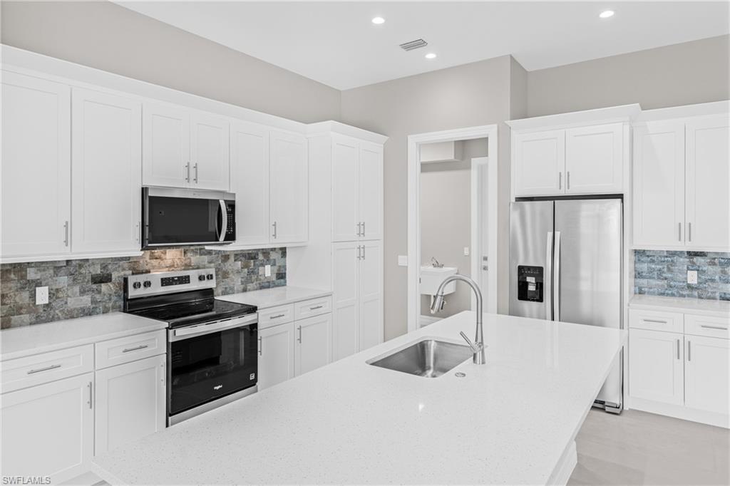 Kitchen featuring tasteful backsplash, appliances with stainless steel finishes, white cabinetry, light stone counters, and recessed lighting